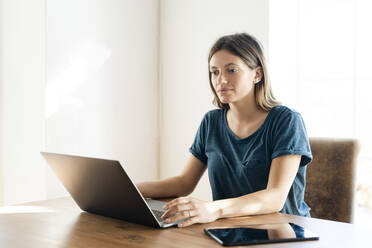 Junge Frau arbeitet zu Hause an ihrem Laptop im Heimbüro - SBOF02254