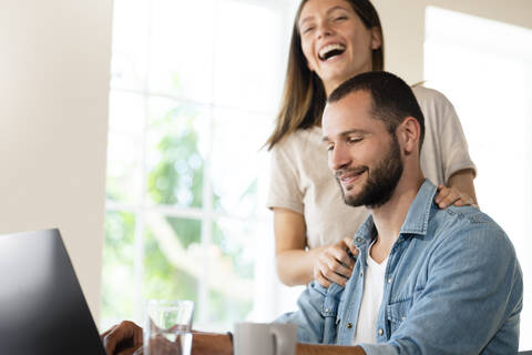 Glückliches junges Paar, das Spaß hat und einen Laptop zu Hause benutzt, lizenzfreies Stockfoto
