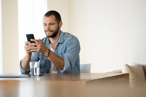 Smiling young man at home checking his smartphone stock photo