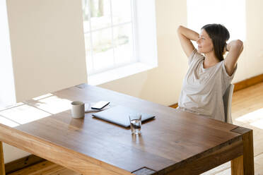 Junge Frau sitzt zu Hause am Tisch im Büro und macht eine Pause - SBOF02271