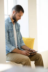 Serious young man at home sitting on window bench checking his smartphone - SBOF02272