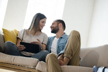 Glückliches junges Paar entspannt sich zu Hause auf der Couch mit Tablet - SBOF02281