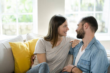 Affectionate young couple in love smiling at each other on couch at home - SBOF02283