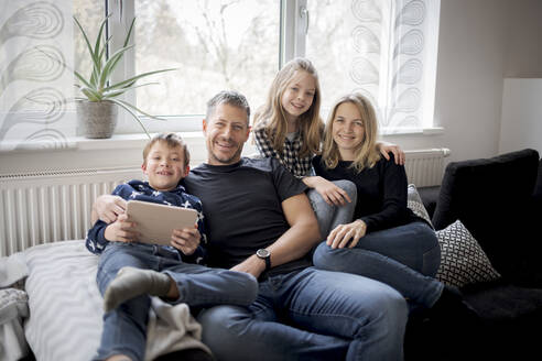 Porträt einer glücklichen Familie, die sich zu Hause auf der Couch entspannt - HMEF00841