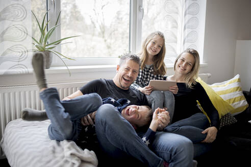 Porträt einer glücklichen Familie, die sich zu Hause auf der Couch amüsiert - HMEF00844