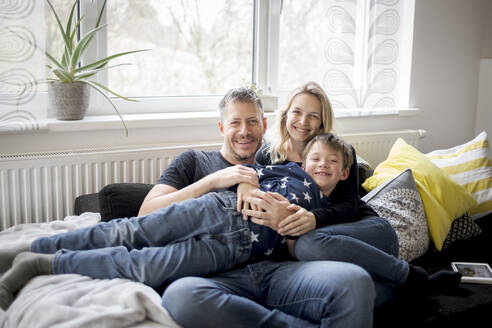 Porträt einer glücklichen Familie, die sich zu Hause auf der Couch entspannt - HMEF00845