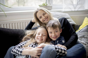 Porträt einer glücklichen Mutter mit Kindern, die sich zu Hause auf der Couch entspannen - HMEF00846