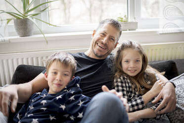 Porträt eines glücklichen Vaters mit Kindern, der sich zu Hause auf der Couch entspannt - HMEF00847