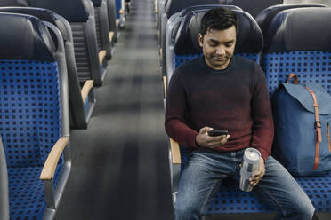 Man holding reusable cup and using smartphone in the train - AHSF02097