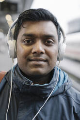 Portrait of smiling man with headphones at the train station - AHSF02100