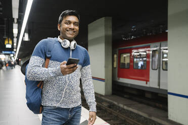 Porträt eines lächelnden Mannes mit Smartphone in einer U-Bahn-Station - AHSF02101