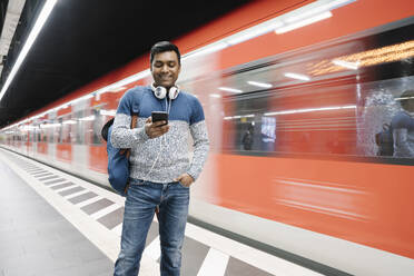 Lächelnder Mann mit Smartphone in einer U-Bahn-Station - AHSF02102