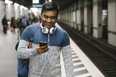 Lächelnder Mann mit Smartphone in einer U-Bahn-Station - AHSF02108