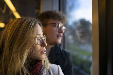Nachdenkliche junge Frau sitzt mit ihrem Freund in der Straßenbahn und schaut aus dem Fenster - FBAF01382