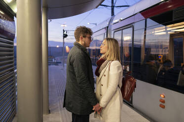 Junges verliebtes Paar steht abends an der Straßenbahnhaltestelle und sieht sich an - FBAF01383