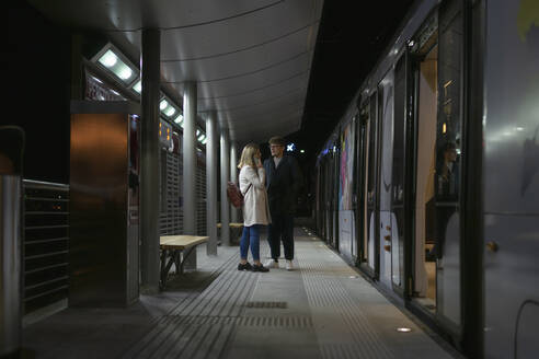 Young couple standing at tram stop in the evening - FBAF01389