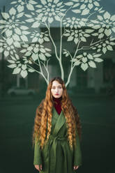 Porträt einer rothaarigen jungen Frau in grünem Mantel vor einer Glasscheibe mit stilisiertem Baum - TCEF00335