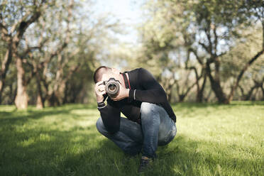 Mann hockt auf einer Wiese und fotografiert mit Kamera - EYAF01015