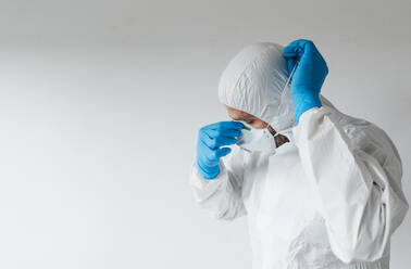 Doctor wearing protective wear, putting on mask - JCMF00520