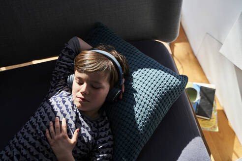 Porträt eines auf der Couch liegenden Jungen, der mit Kopfhörern Musik hört - AUF00247