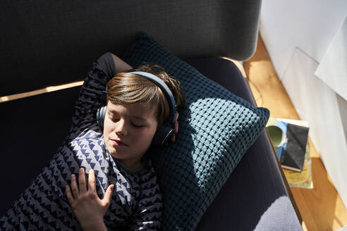 Portrait of boy lying on couch listening music with headphones - AUF00247