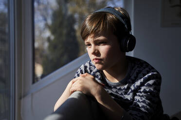 Porträt eines nachdenklichen Jungen, der mit Kopfhörern Musik hört und aus dem Fenster schaut - AUF00248