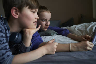 Geschwister liegen zusammen auf dem Bett und benutzen ihr Smartphone für einen Videochat - AUF00256