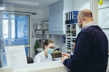 Employee at reception desk of hospital ward and visitor - MFF05290