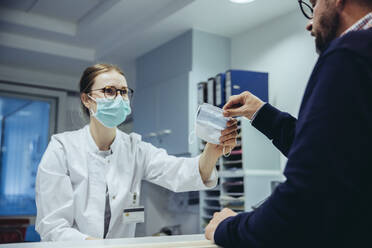 Employee at reception desk of hospital ward handing over mask to visitor - MFF05293