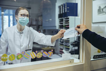 Angestellter an der Rezeption einer Krankenstation übergibt einem Besucher eine Maske - MFF05295