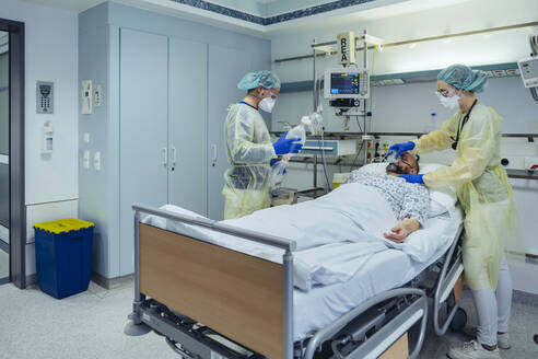 Doctors caring for patient in emergency care unit of a hospital changing breathing from oxygen mask to bag valve mask - MFF05338