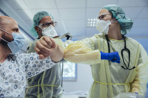 Ärzte stoßen mit dem Ellbogen an einen geheilten Patienten in der Notaufnahme eines Krankenhauses - MFF05350
