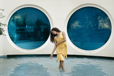 Junge Frau im gelben Sommerkleid tanzt im Pool - TCEF00372
