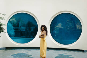 Young woman wearing yellow summer dress standing in pool - TCEF00373