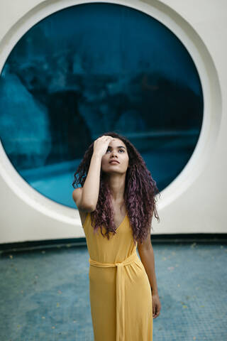 Portrait of young woman wearing yellow summer dress standing in pool looking up stock photo