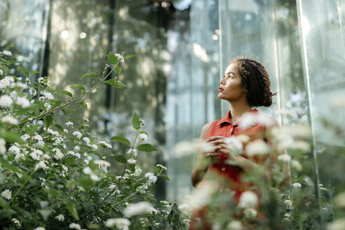 Porträt einer nachdenklichen jungen Frau, die in einem städtischen Garten steht und nach oben schaut - TCEF00380