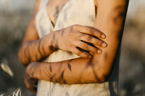 Crop view of woman at sunset with shadows of leaves on her arms - TCEF00394