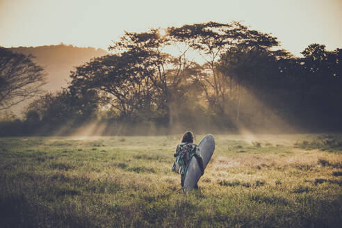 Rückenansicht eines jungen Surfers auf dem Weg zum Strand bei Sonnenaufgang, Costa Rica - AMUF00031