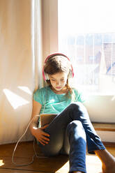 Girl sitting on the floor at home using headphones and digital tablet - LVF08727