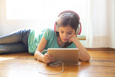 Mädchen, das zu Hause auf dem Boden liegt und Kopfhörer und ein digitales Tablet benutzt - LVF08728