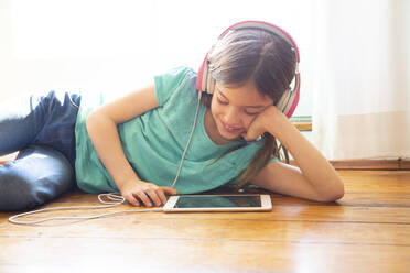 Girl lying on the floor at home using headphones and digital tablet - LVF08729