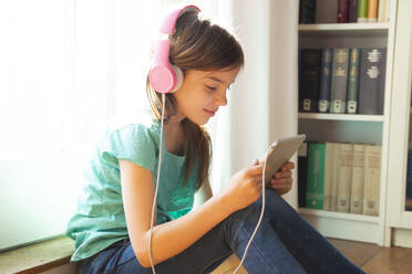 Smiling girl sitting on the floor at home using headphones and digital tablet - LVF08730