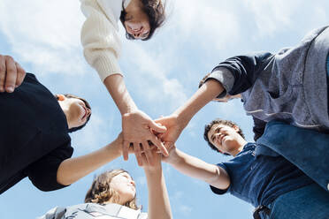 Five friends stacking their hands looking at each other, seen from below - JCMF00534