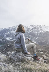 Rückenansicht einer jungen Frau, die auf einem Felsen sitzt und die Aussicht betrachtet, Provinz Leon, Spanien - FVS00003