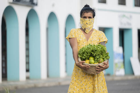 Frau mit Mundtuch hält Korb mit Salat und frischen Früchten - AMUF00033
