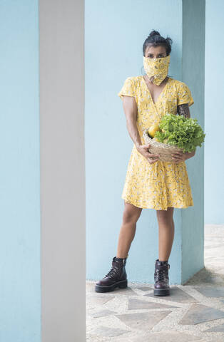 Woman wearing mouth cloth holding basket with salad and fresh fruits stock photo