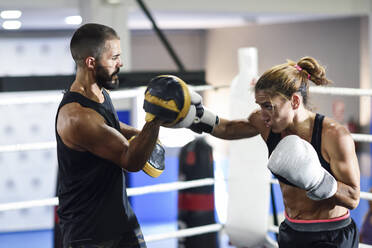 Weibliche Boxerin beim Sparring mit ihrem Trainer im Fitnessstudio - JSMF01513