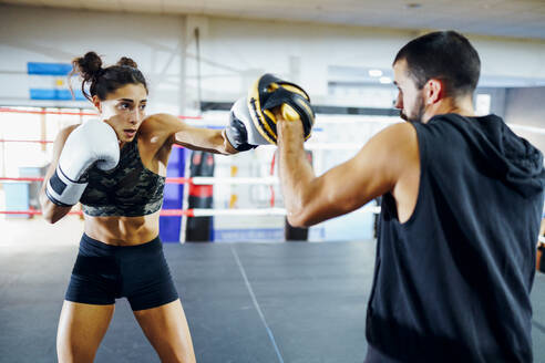 Weibliche Boxerin beim Sparring mit ihrem Trainer im Fitnessstudio - JSMF01533