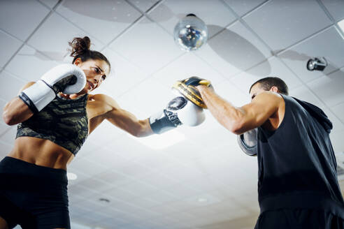 Weibliche Boxerin beim Sparring mit ihrem Trainer im Fitnessstudio - JSMF01534