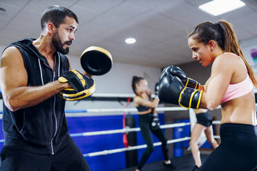 Weibliche Boxerin beim Sparring mit ihrem Trainer im Fitnessstudio - JSMF01535